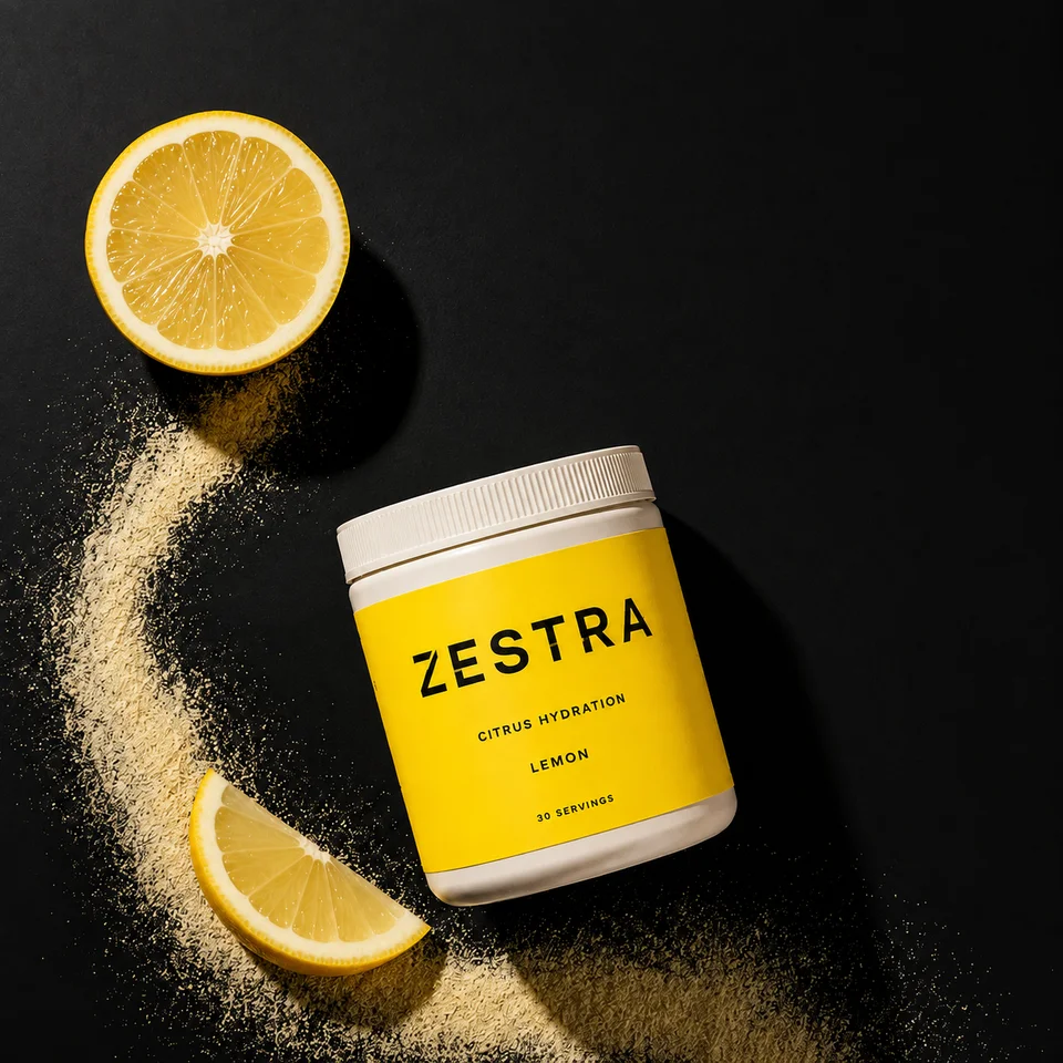 Overhead ZESTRA lemon hydration concept with a bright lemon-yellow label, fresh lemons and a curved sweep of powder